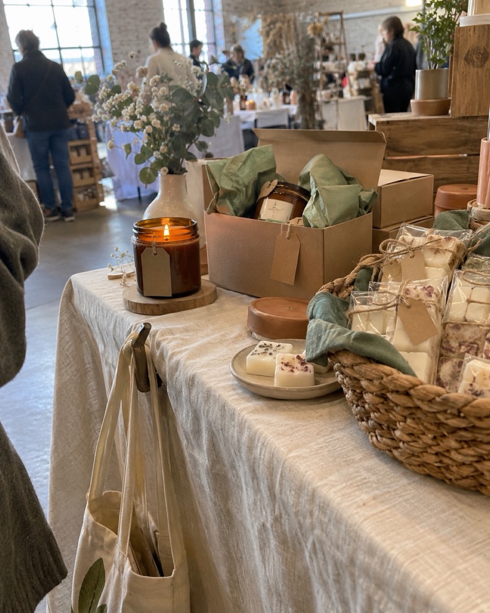 A small craft market table with labeled soy jar candles on display